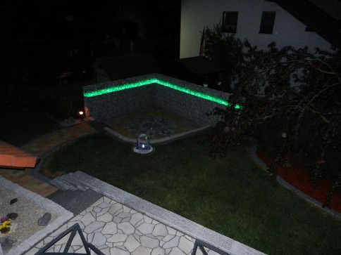 Fertige Terrasse mit beleuchtetem Gabionenaufbau in der Farbe grün leuchtend